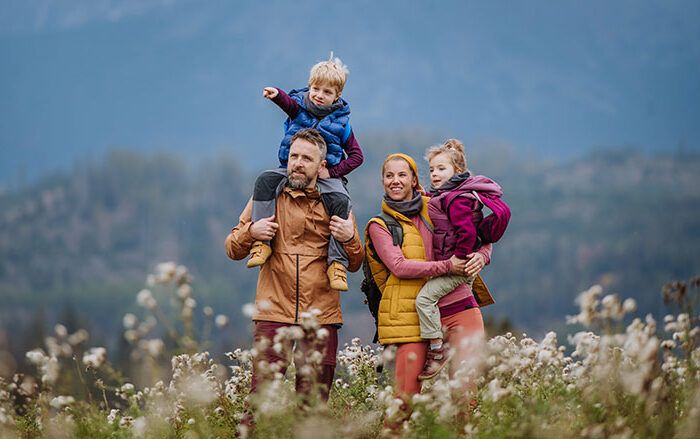 Happy parents with their little kids on piggyback at autumn walk.